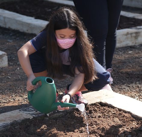 Criança molhando a terra com regador no Projeto Horta